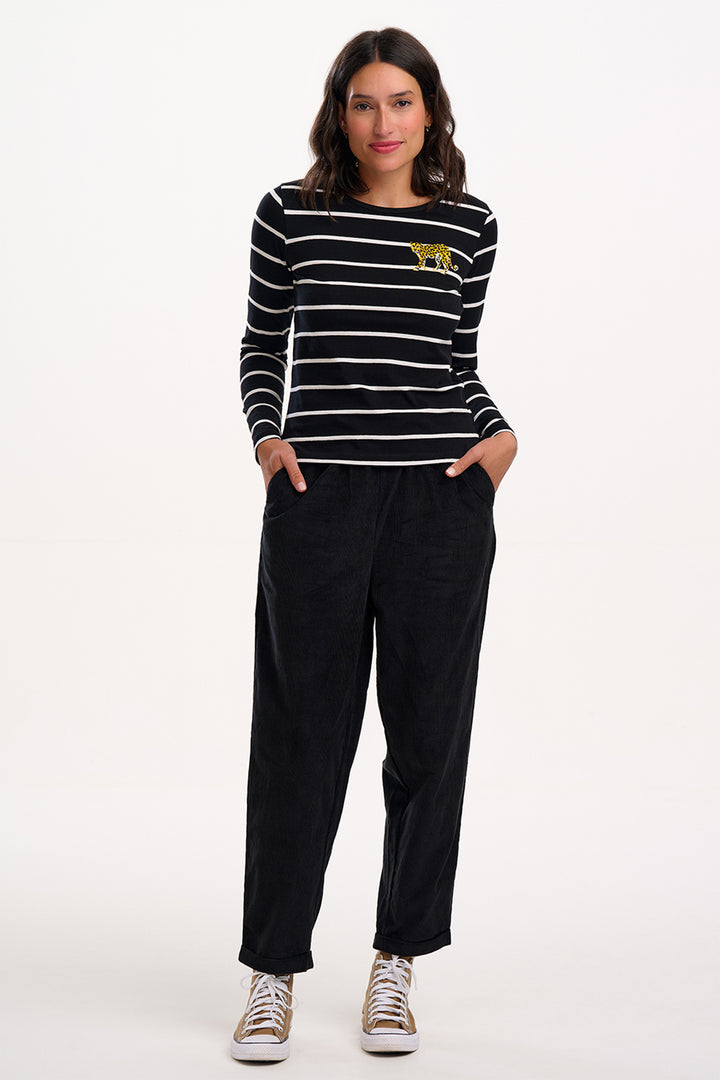 Woman wearing a black and white striped shirt with a yellow logo and black pants on a white background