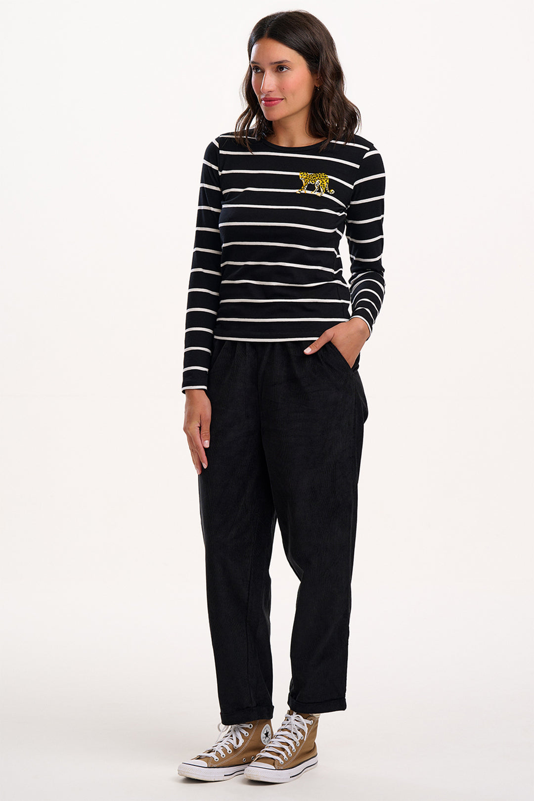 Woman wearing a black and white striped shirt with a yellow logo and black pants on a white background