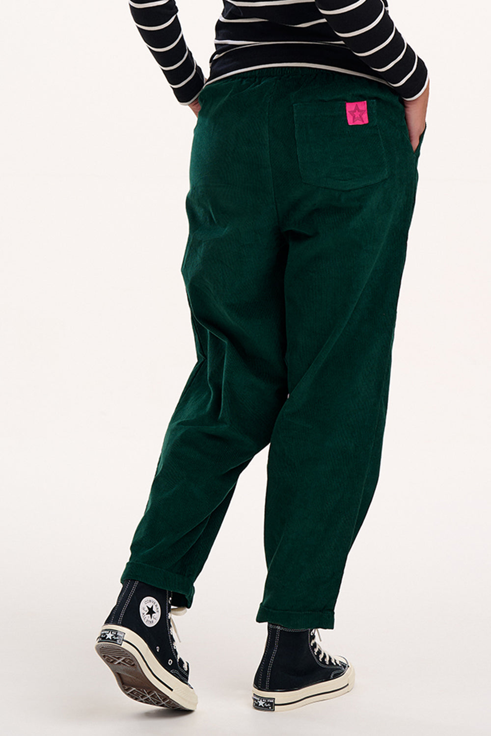 Person wearing green pants with a pink label, black and white striped shirt, and black sneakers on a white background