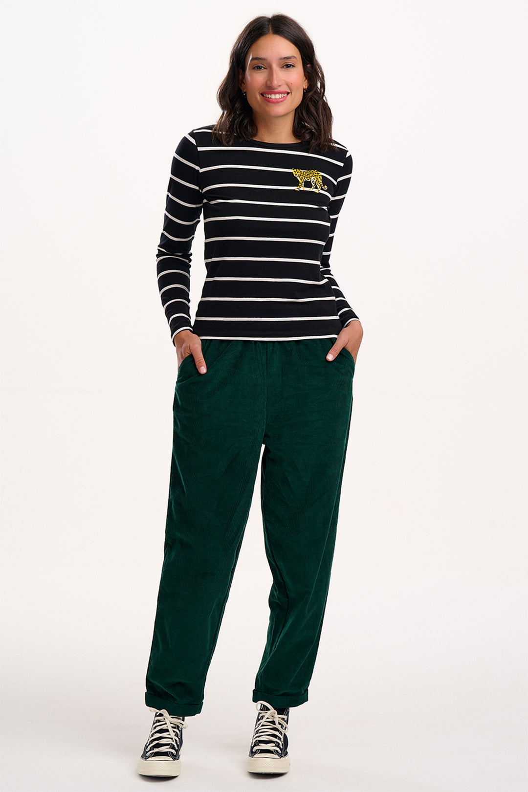Woman wearing a black and white striped shirt with a yellow logo and green pants on a white background