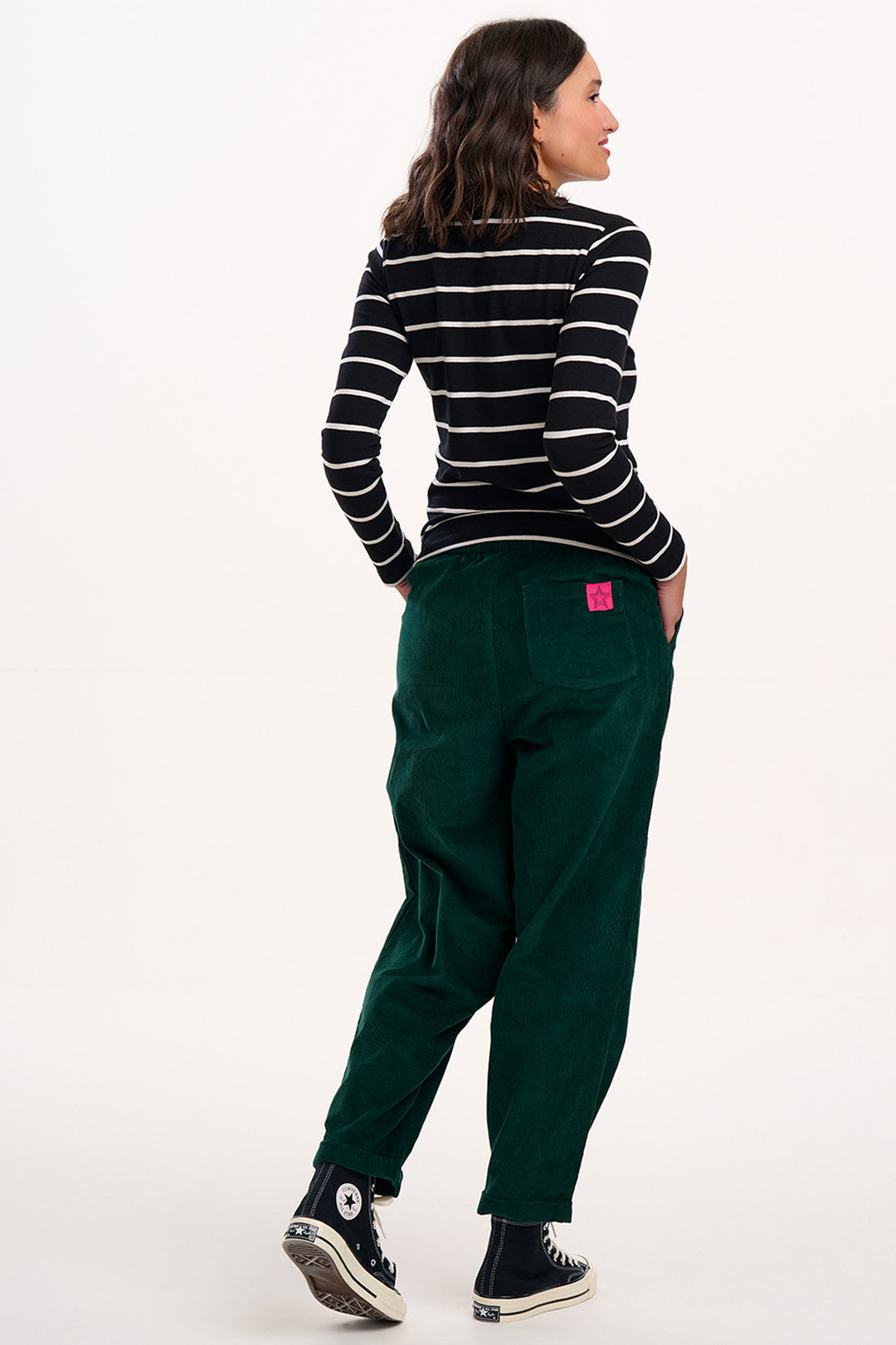 Person wearing a striped shirt and green pants with a pink tag on a white background