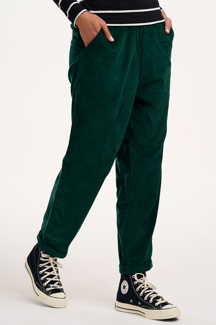 Person wearing green pants and black sneakers on a white background