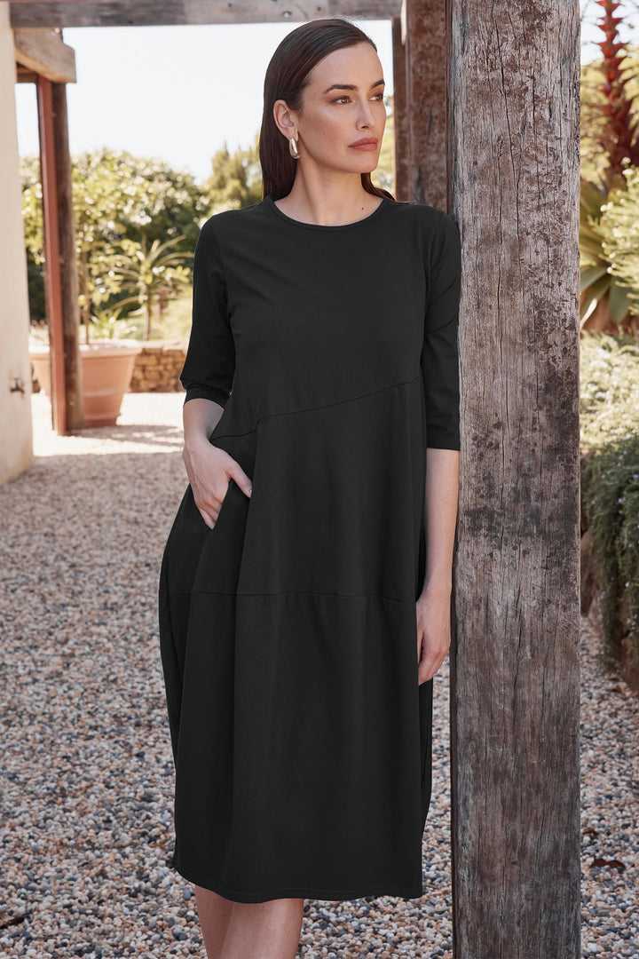 Woman wearing a black dress standing outdoors near a wooden post.