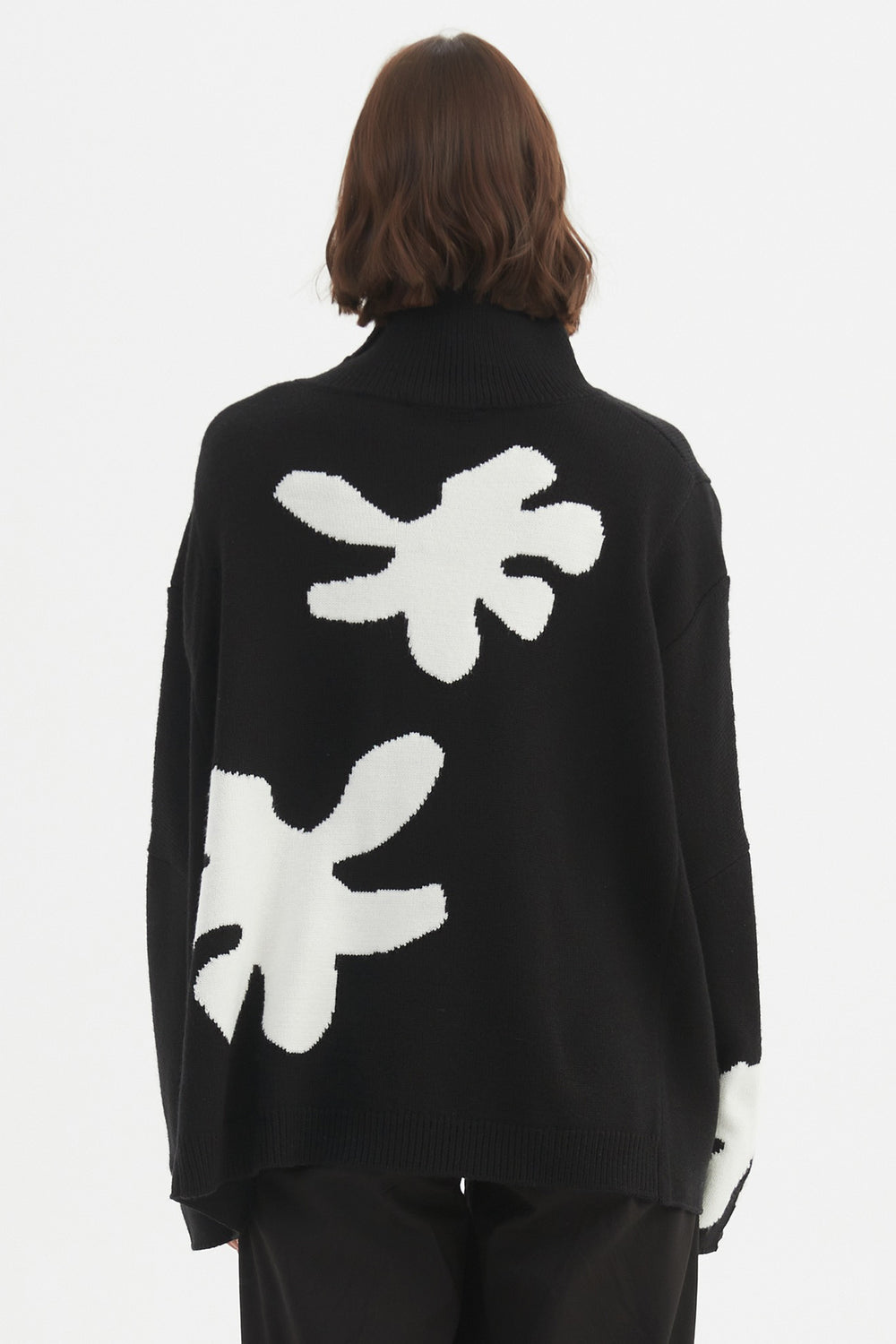 Person wearing a black sweater with white abstract designs on the back against a white background