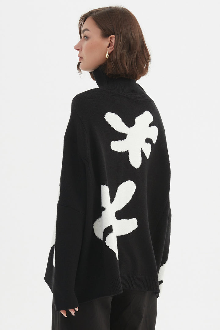 Person wearing a black cardigan with white floral patterns on the back, standing against a plain background.