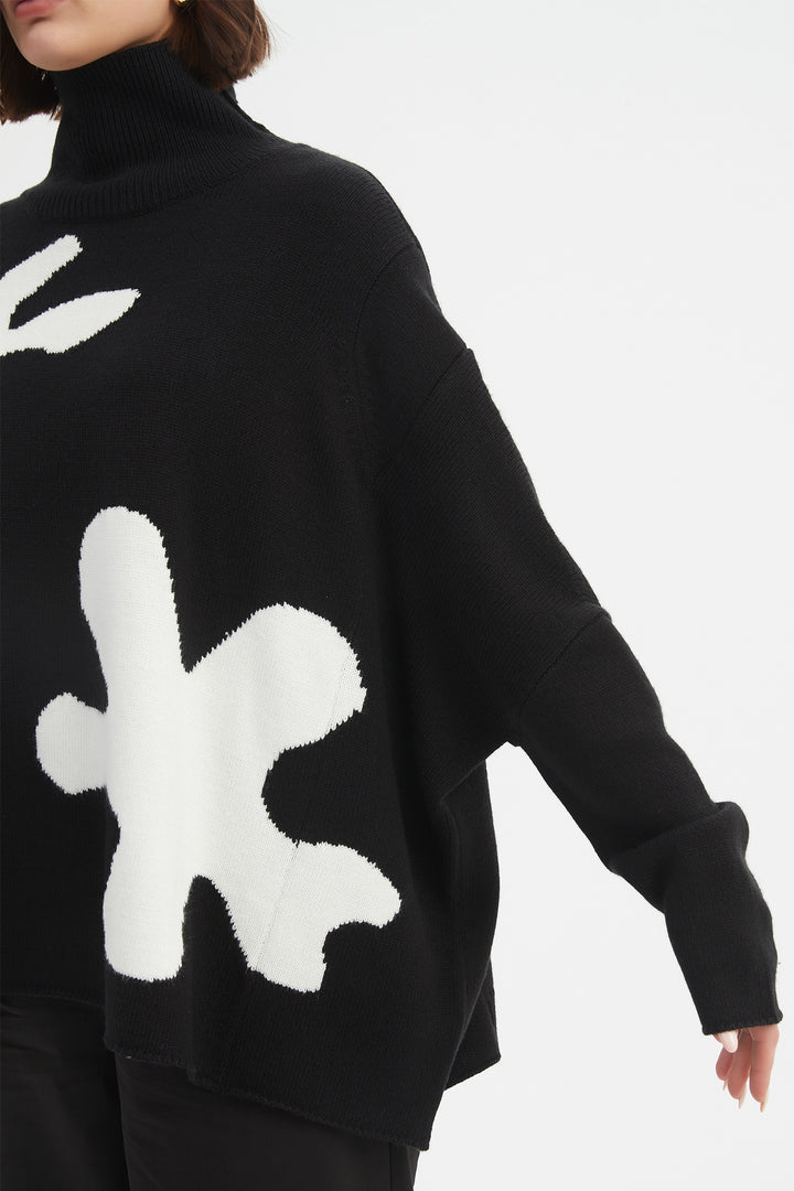Black sweater with white abstract patterns worn by a person on a light gray background