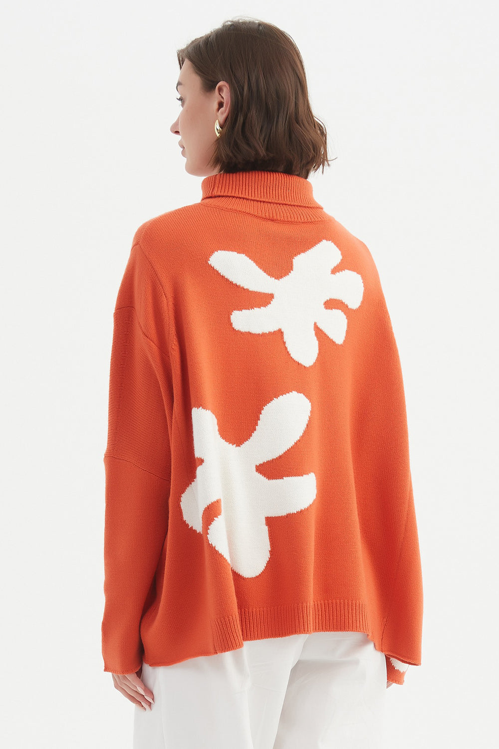 Person wearing an orange sweater with white floral patterns on a plain background