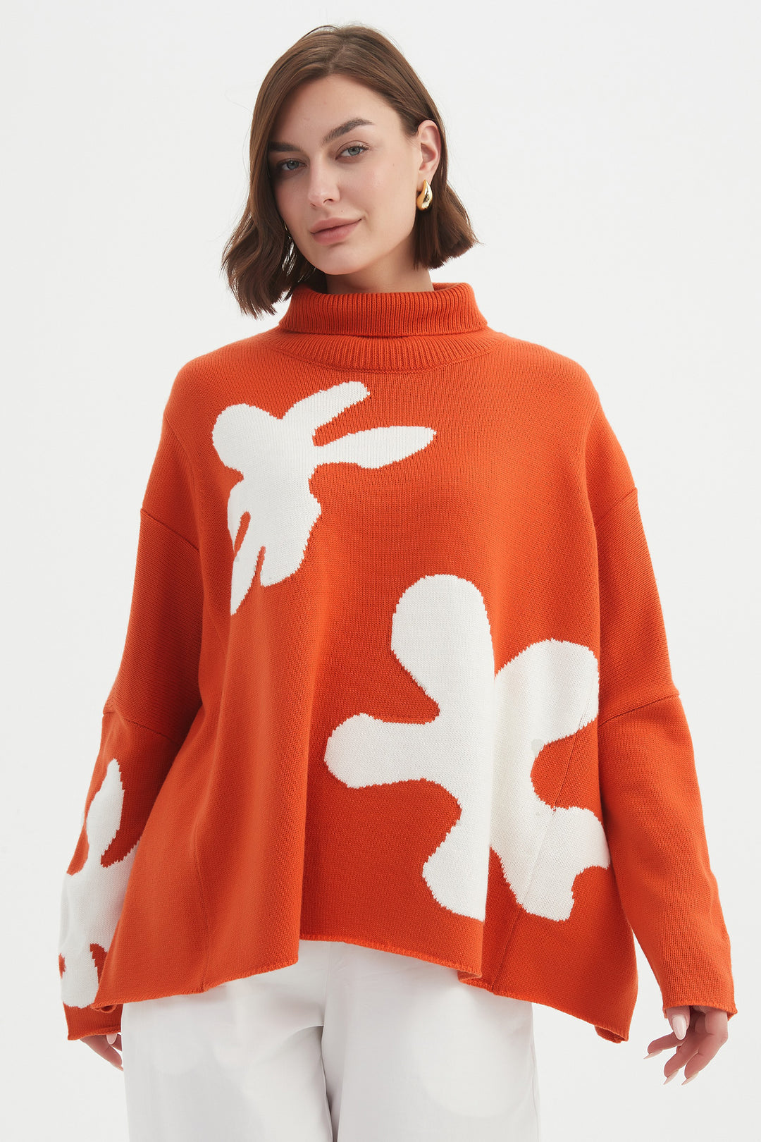 Woman wearing an orange sweater with white floral patterns on a white background