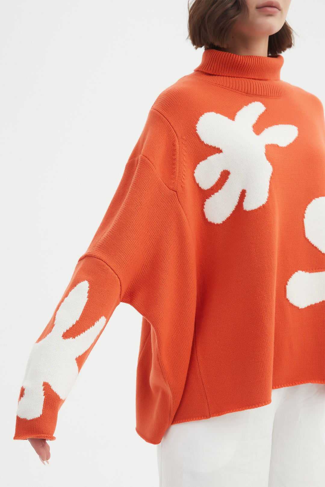Orange sweater with white abstract patterns worn by a person on a white background