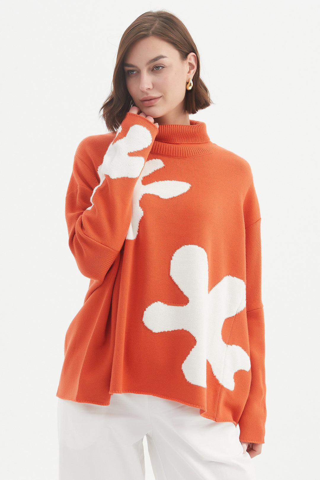 Person wearing an orange sweater with white floral patterns on a white background