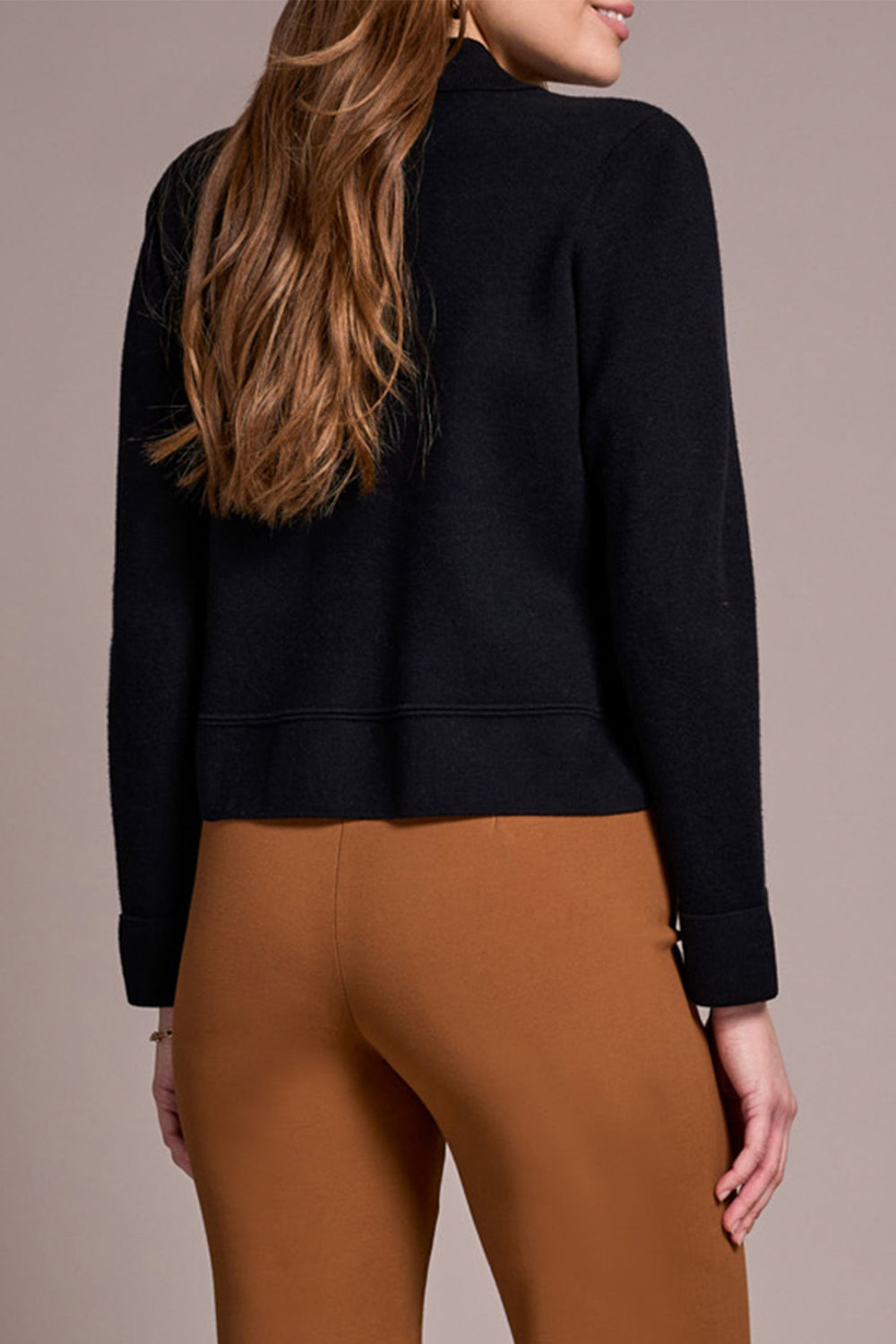 Person wearing a black sweater and brown pants on a beige background