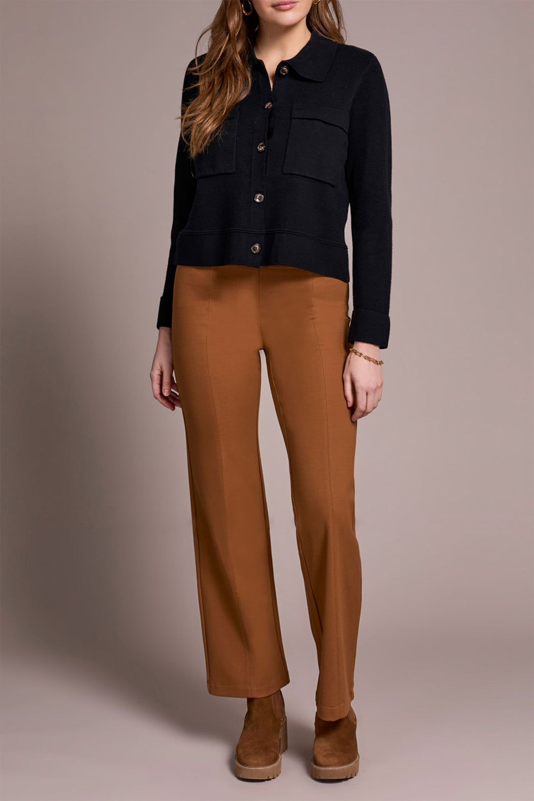 Person wearing a black jacket and brown pants on a neutral background
