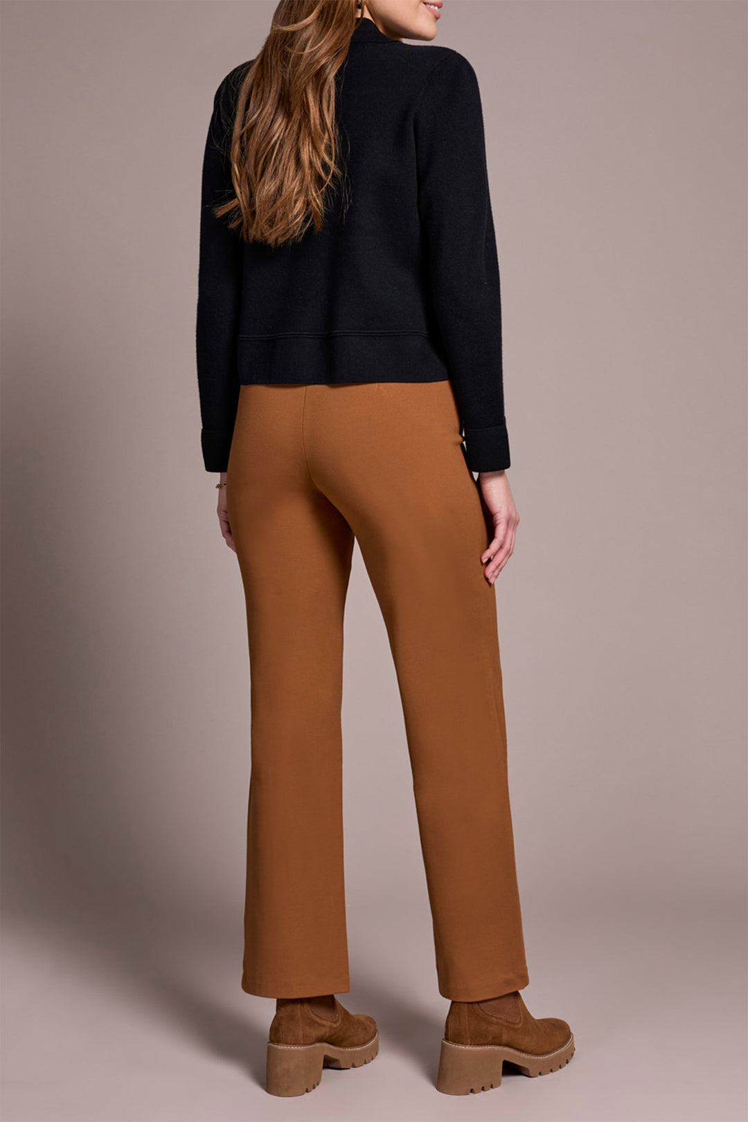 Person wearing a black top and brown pants on a beige background