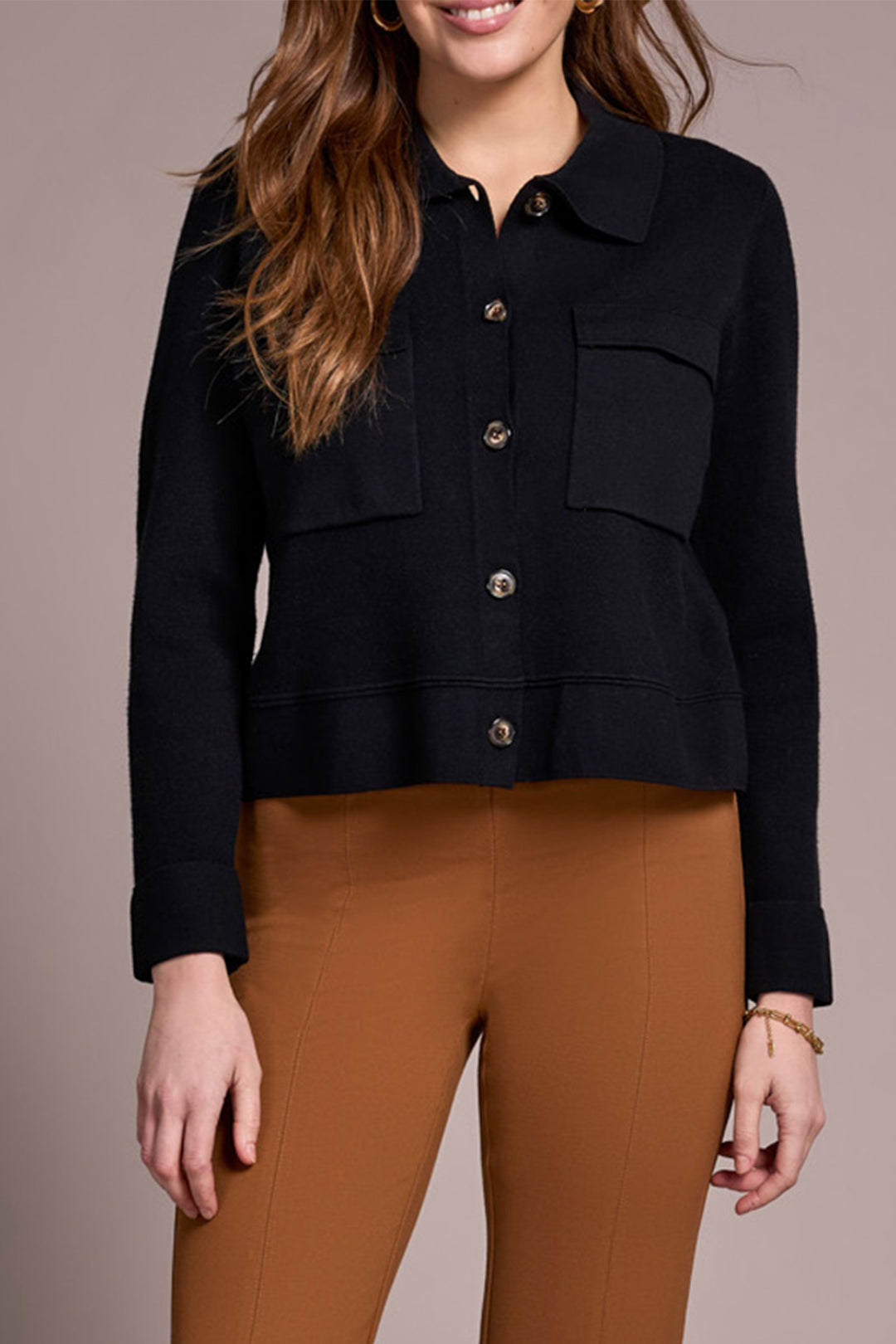 Woman wearing a black jacket and brown pants on a beige background