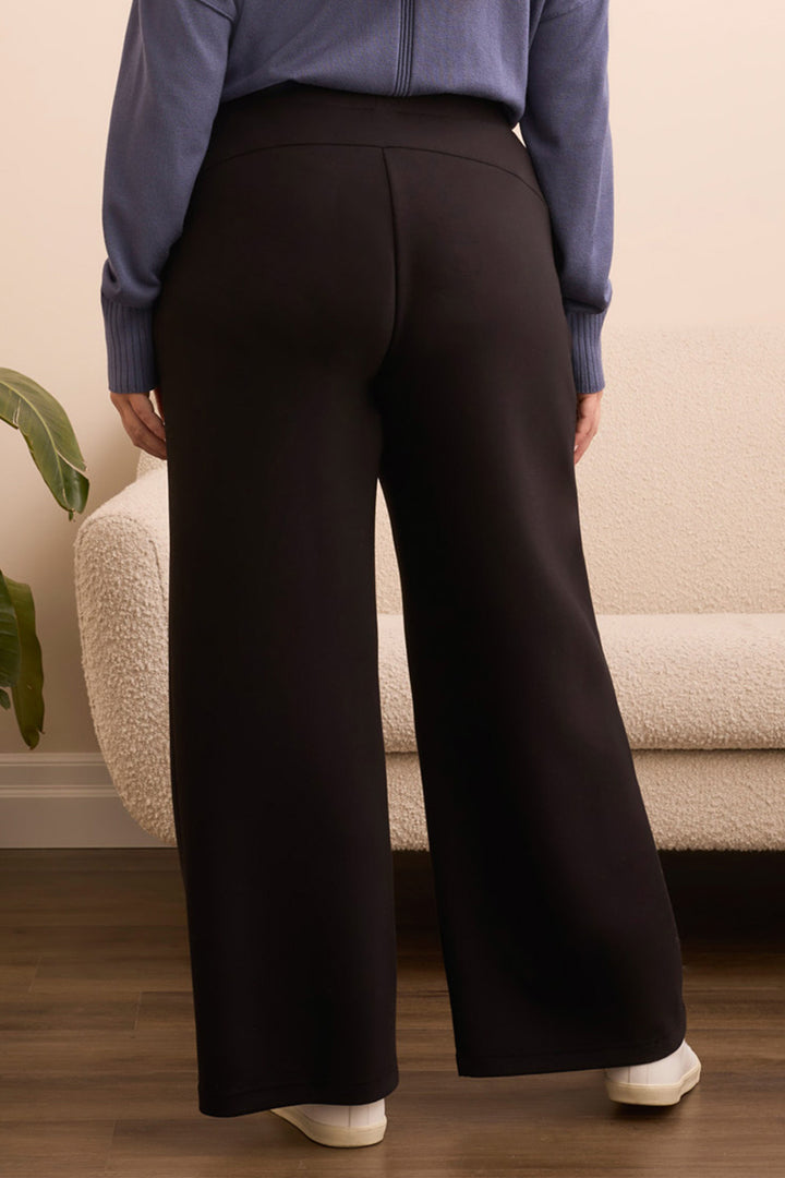 Person wearing black wide-leg pants and a blue top in a room with a beige sofa and plant.