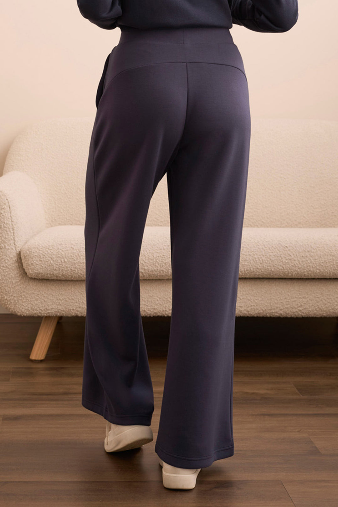 Person wearing dark blue pants standing in a room with a beige sofa.