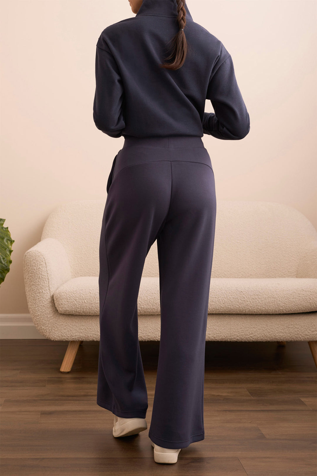 Person wearing a navy outfit standing in a room with a beige sofa and wooden floor.