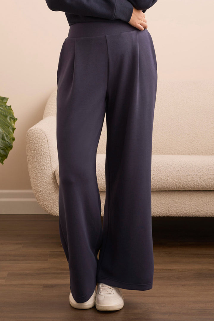 Person wearing dark blue pants standing in a room with a beige couch and plant.