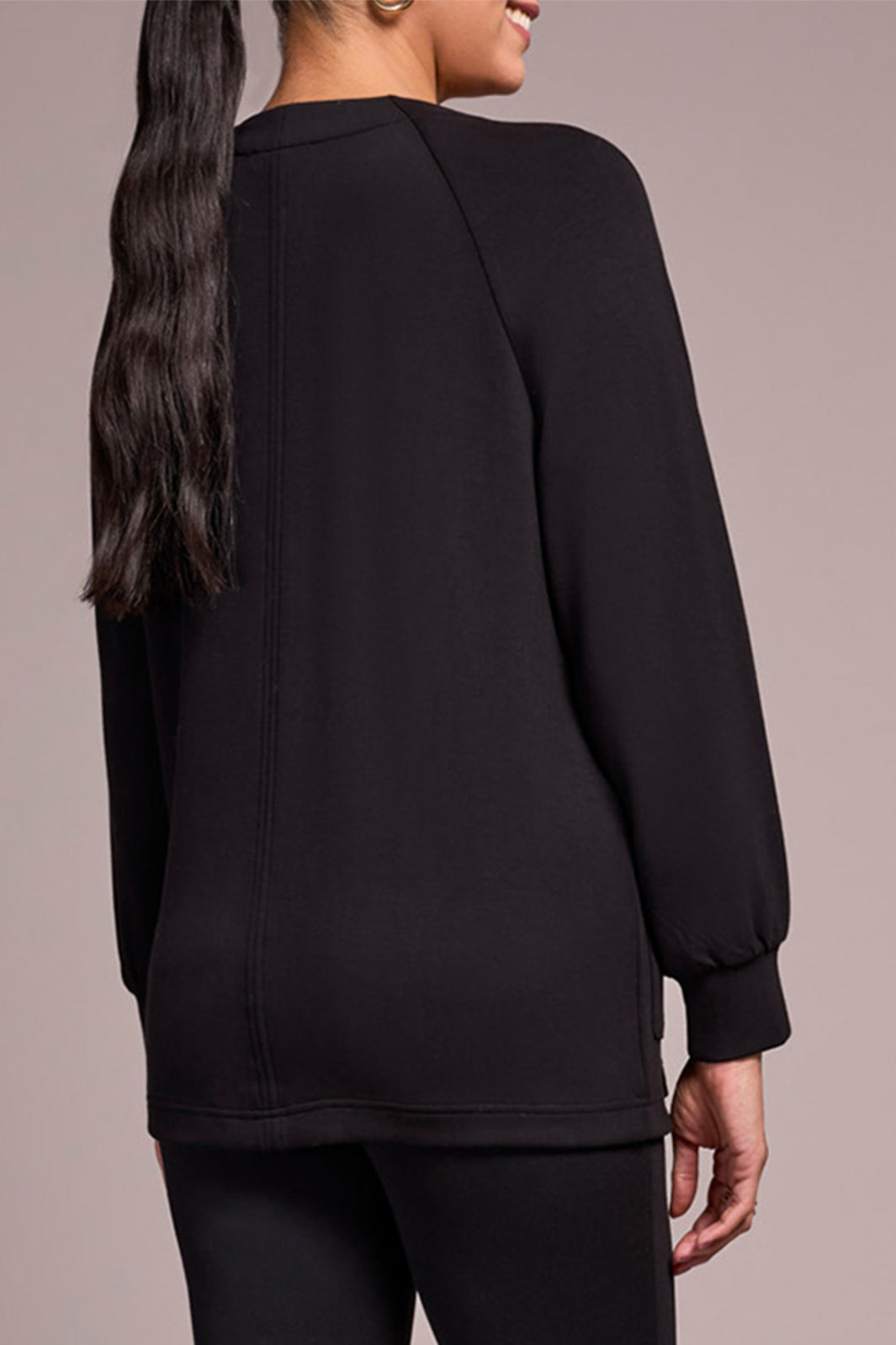 Person wearing a black long-sleeve top against a neutral background