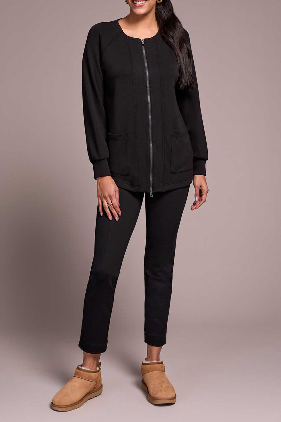 Person wearing a black outfit with beige boots on a plain background