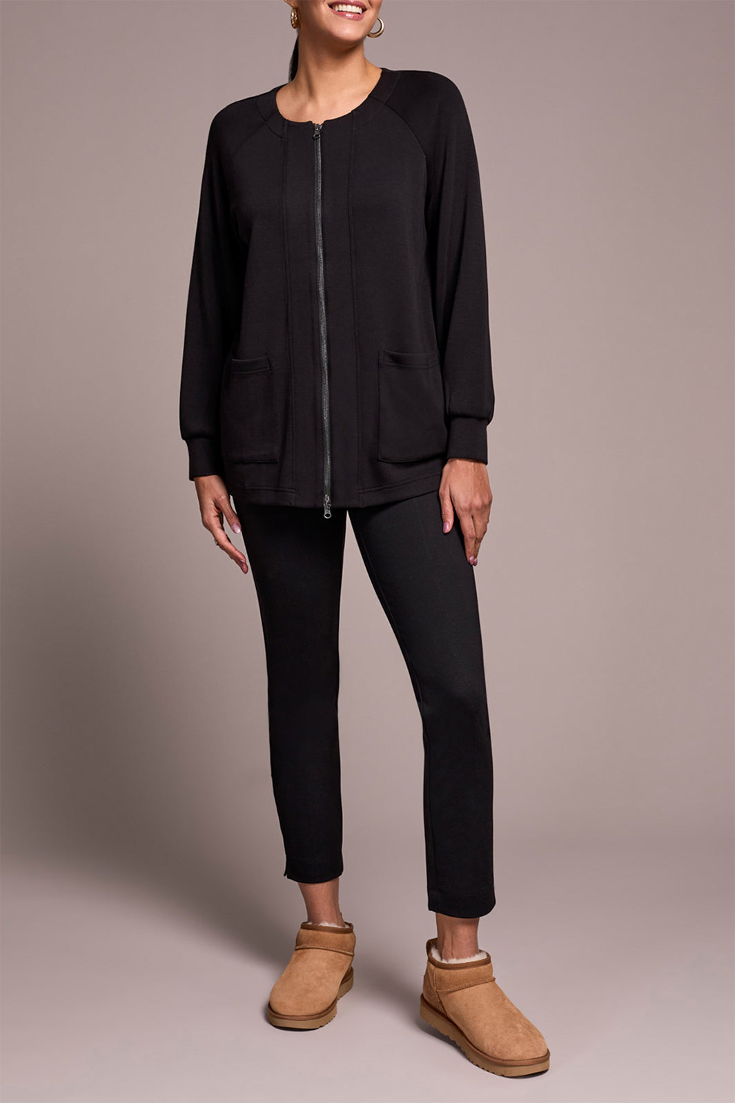 Person wearing a black outfit with brown shoes on a plain background