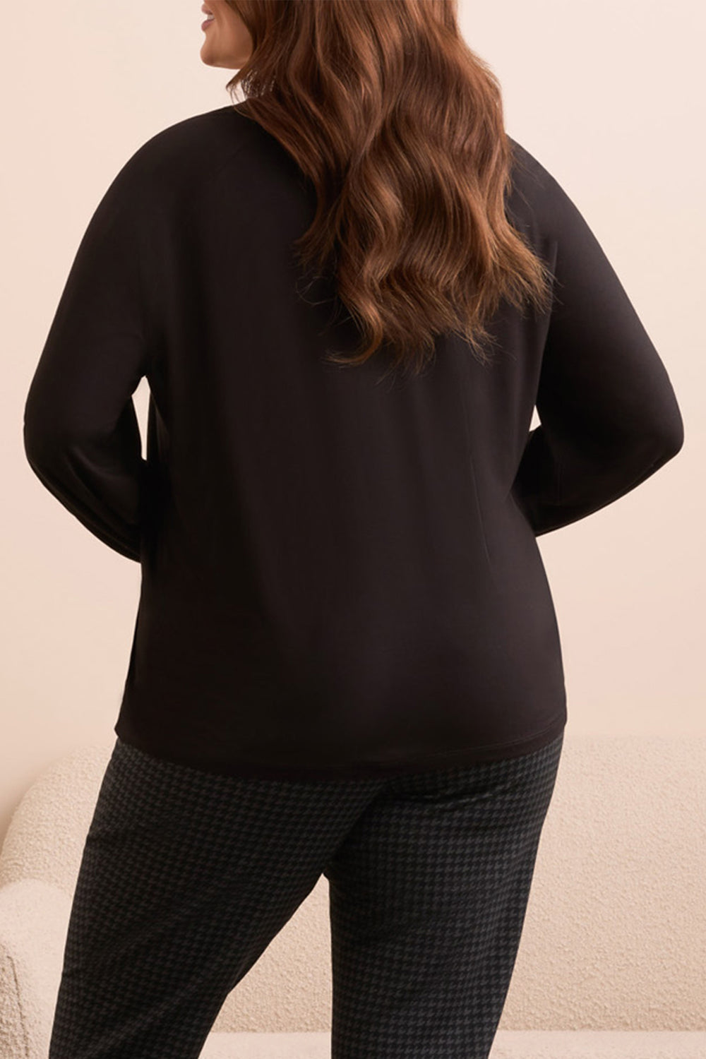 Person wearing a black top and plaid pants on a beige background