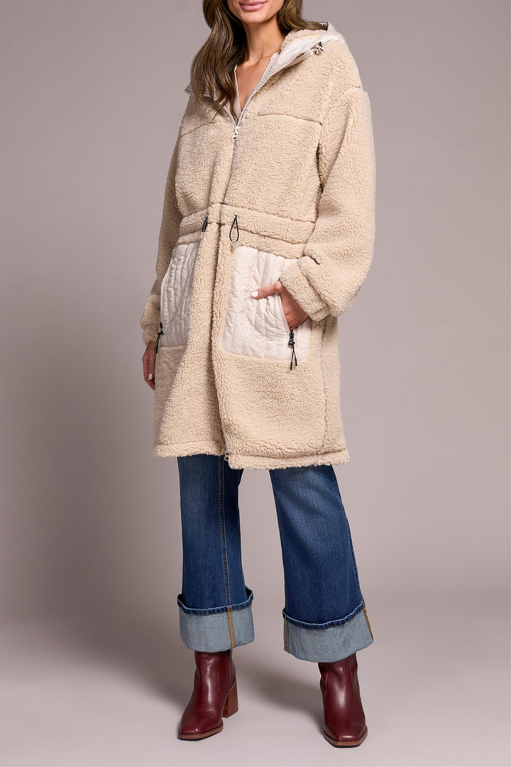 Person wearing a beige fleece-lined coat with a plain background