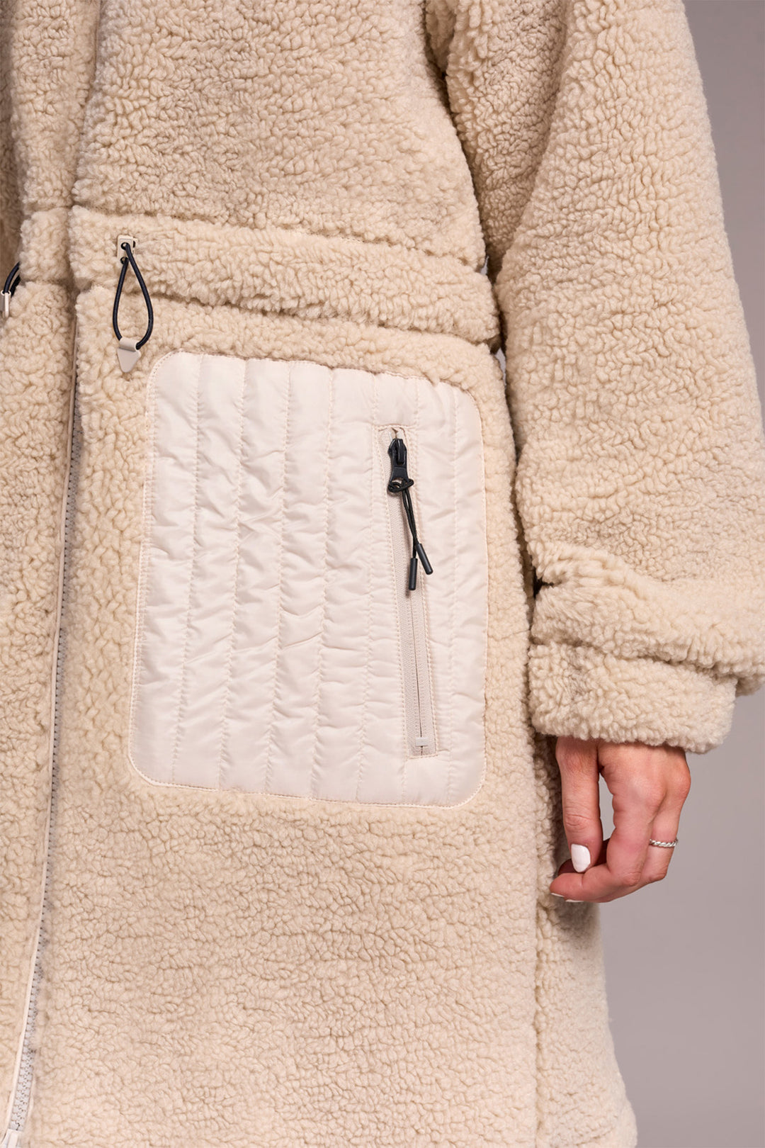Close-up of a beige fleece jacket with a pocket and zipper detail.