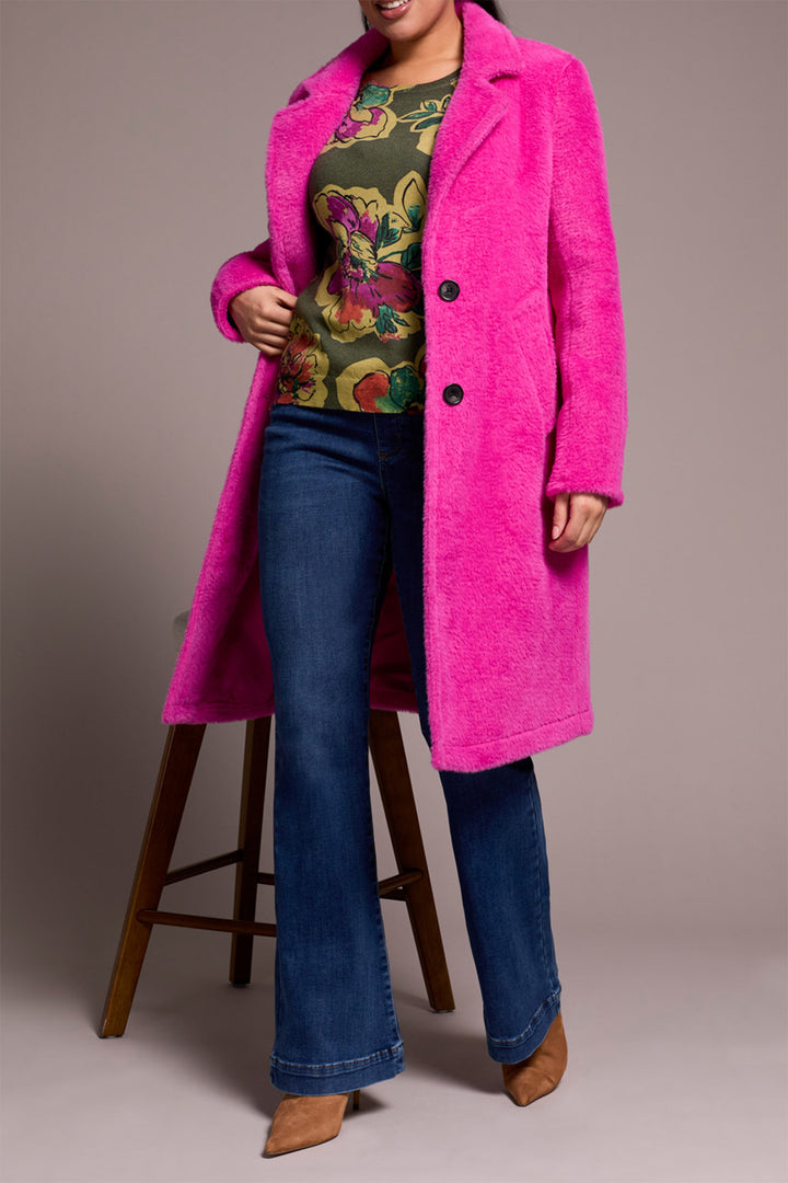 Person wearing a bright pink coat over a colorful top and blue jeans on a plain background