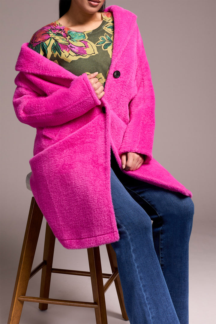 Person wearing a bright pink coat sitting on a wooden stool against a neutral background