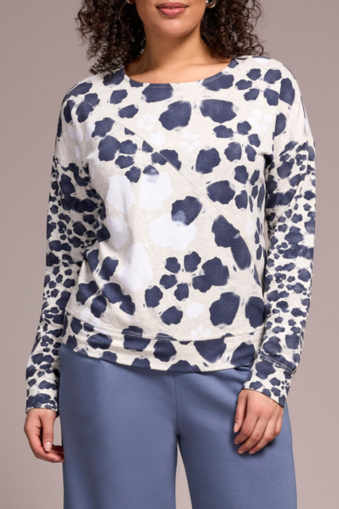 Person wearing a white long-sleeve shirt with blue leopard print and blue pants on a beige background