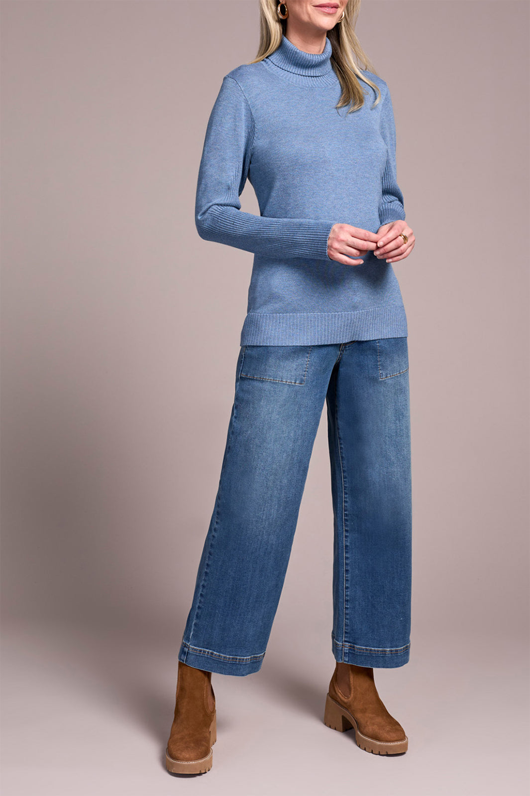 Person wearing a blue sweater and jeans with brown boots on a plain background