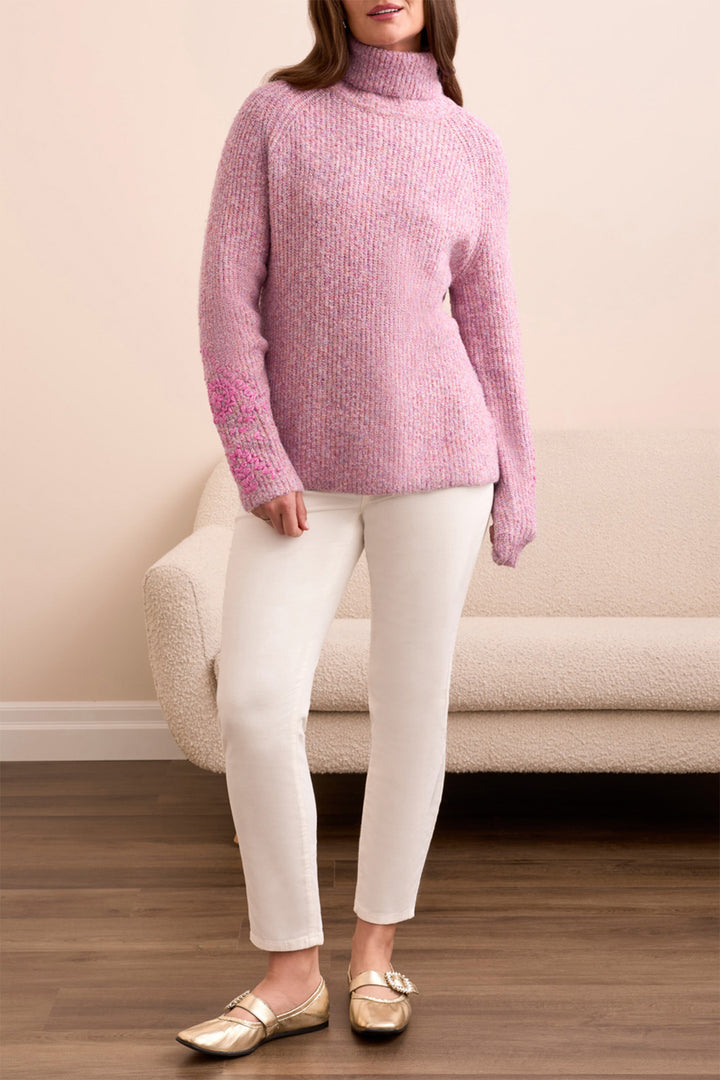 Person wearing a pink sweater and white pants sitting on a beige couch.