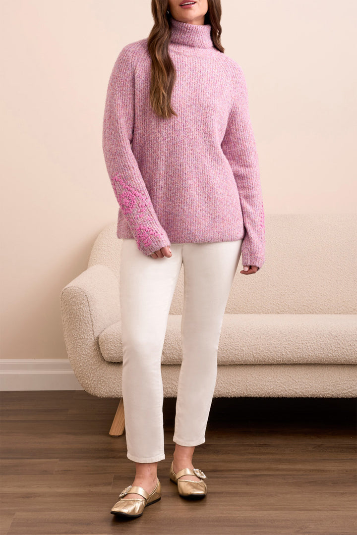 Person wearing a pink sweater and white pants standing in a room with a beige couch.