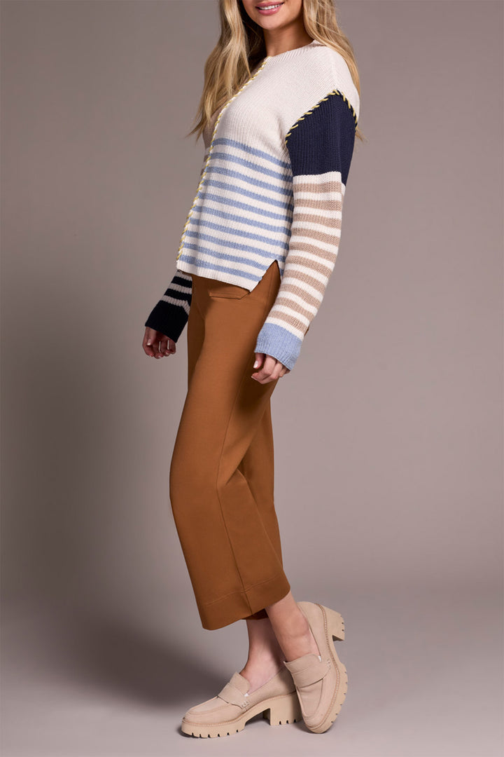 Woman wearing a striped sweater and brown pants on a plain background