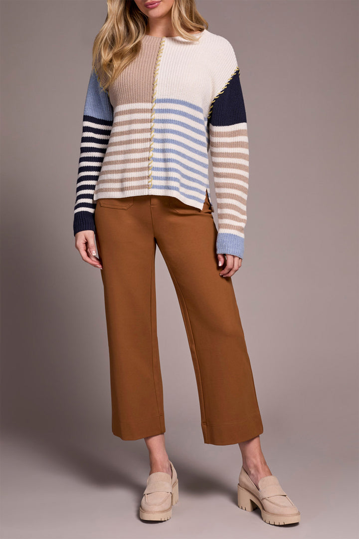 Woman wearing a striped sweater and brown pants on a plain background