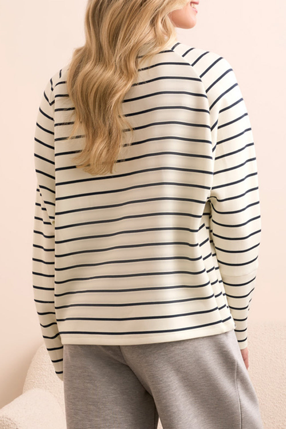 Person wearing a striped long-sleeve shirt and gray pants against a beige background