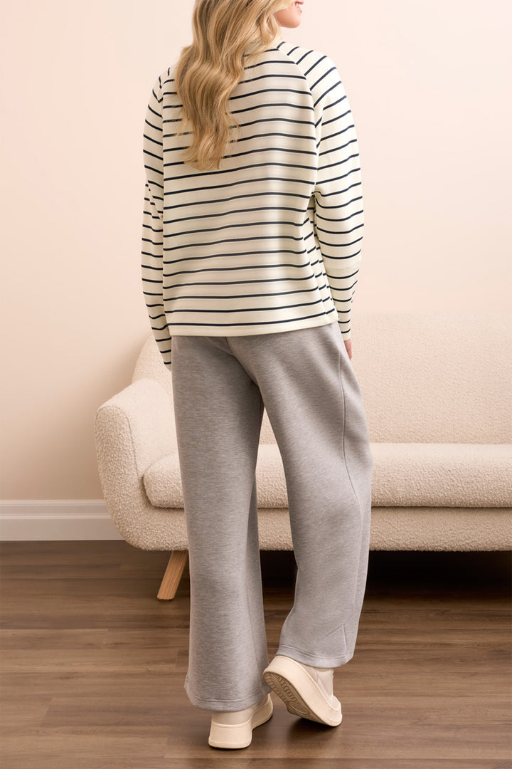 Person wearing a striped sweater and gray pants standing in a room with a beige couch.