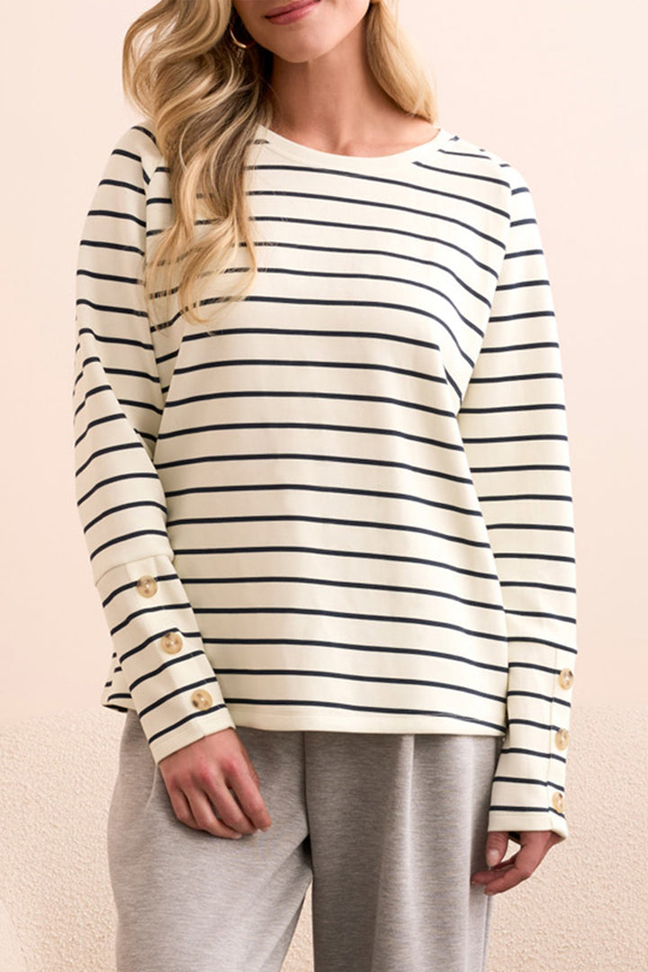 Woman wearing a striped long-sleeve top and gray pants on a beige background