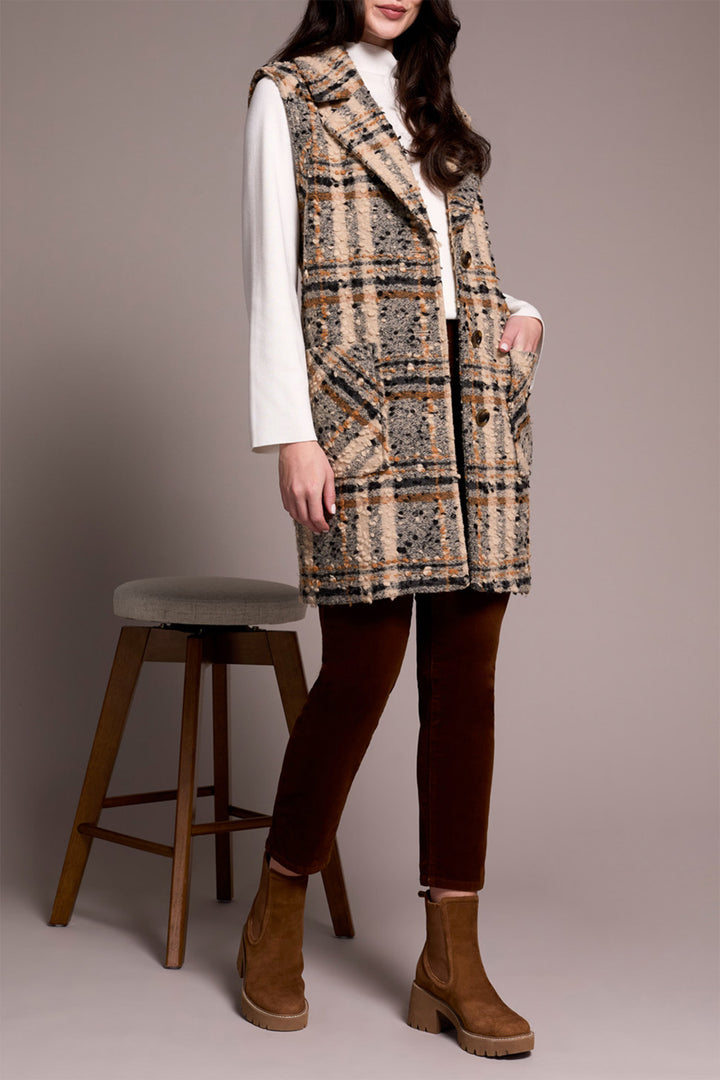 Person wearing a plaid vest over a white shirt, brown pants, and brown boots on a plain background.