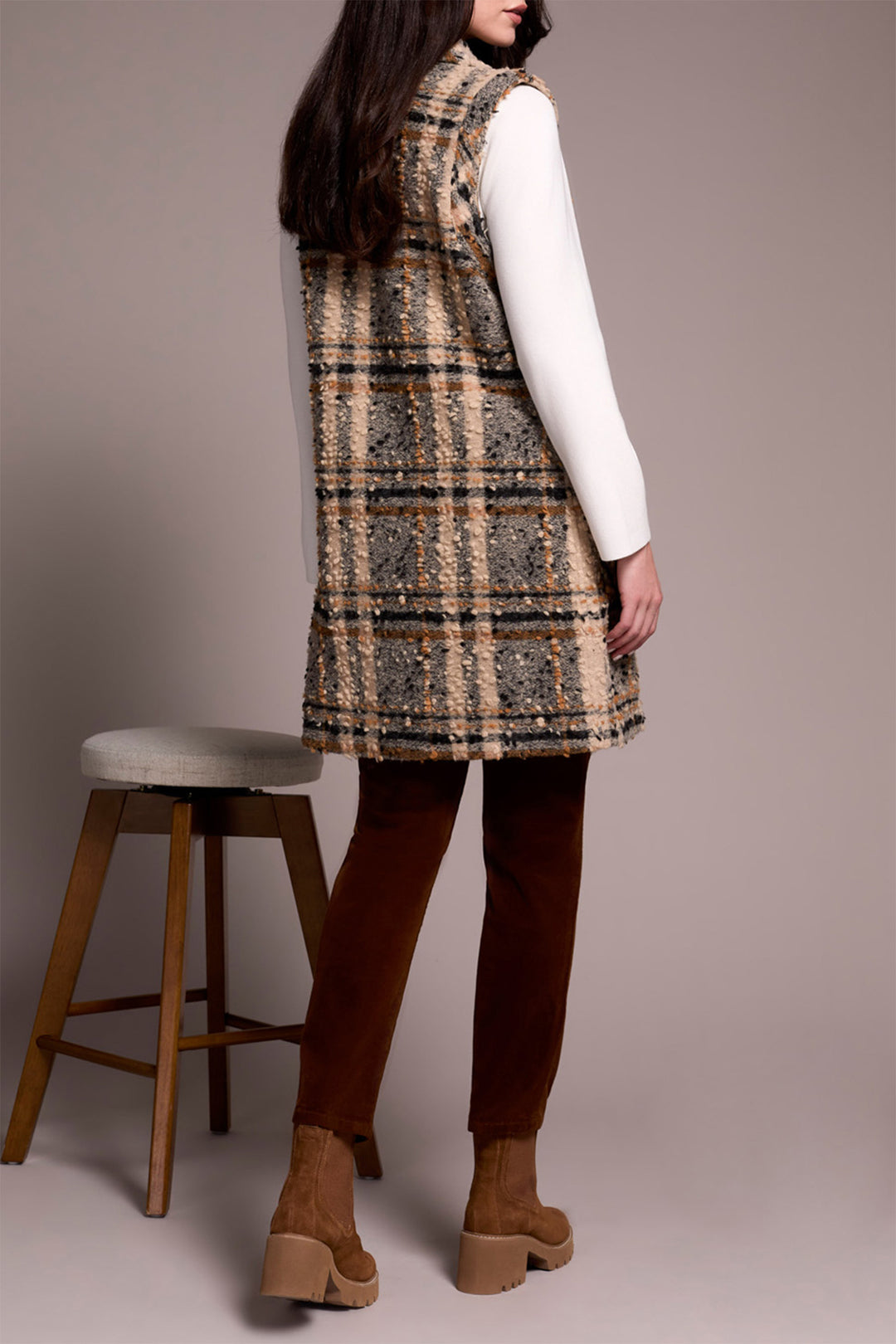 Person wearing a plaid vest over a white shirt with brown pants and shoes, standing against a plain background.