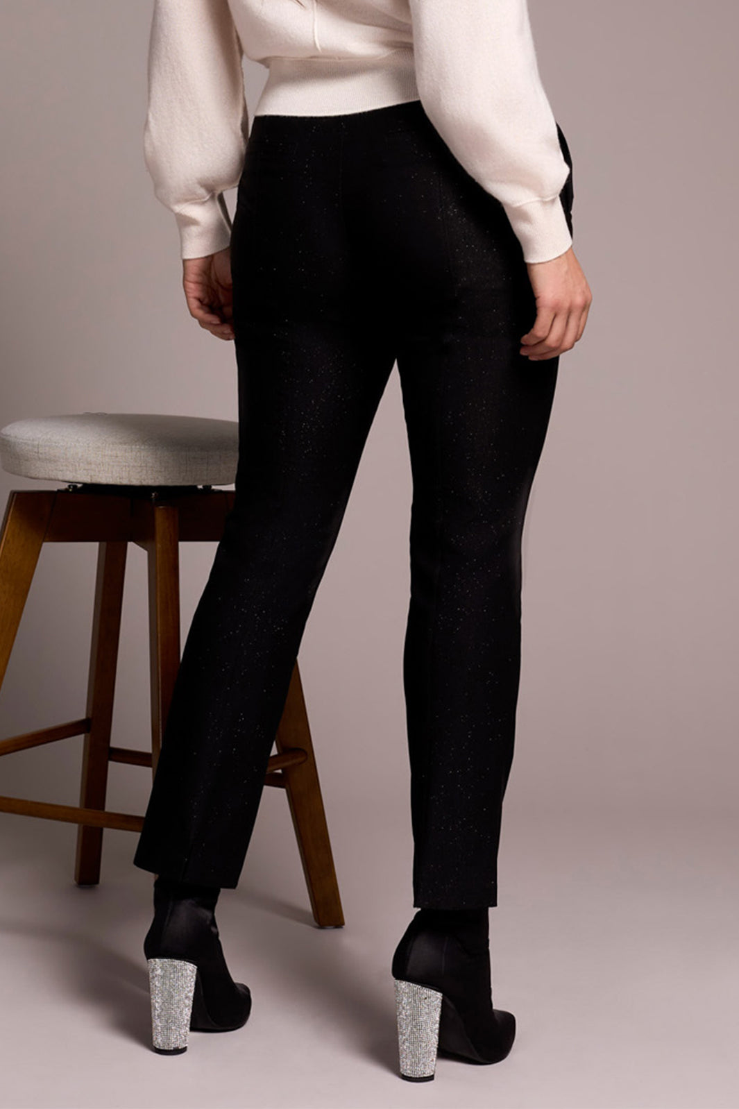 Person wearing black pants and white shirt standing next to a wooden stool on a plain background