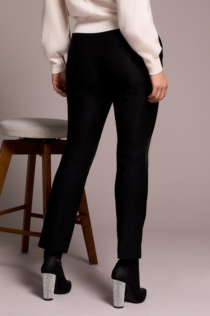 Person wearing black pants and white shirt standing next to a wooden stool on a plain background