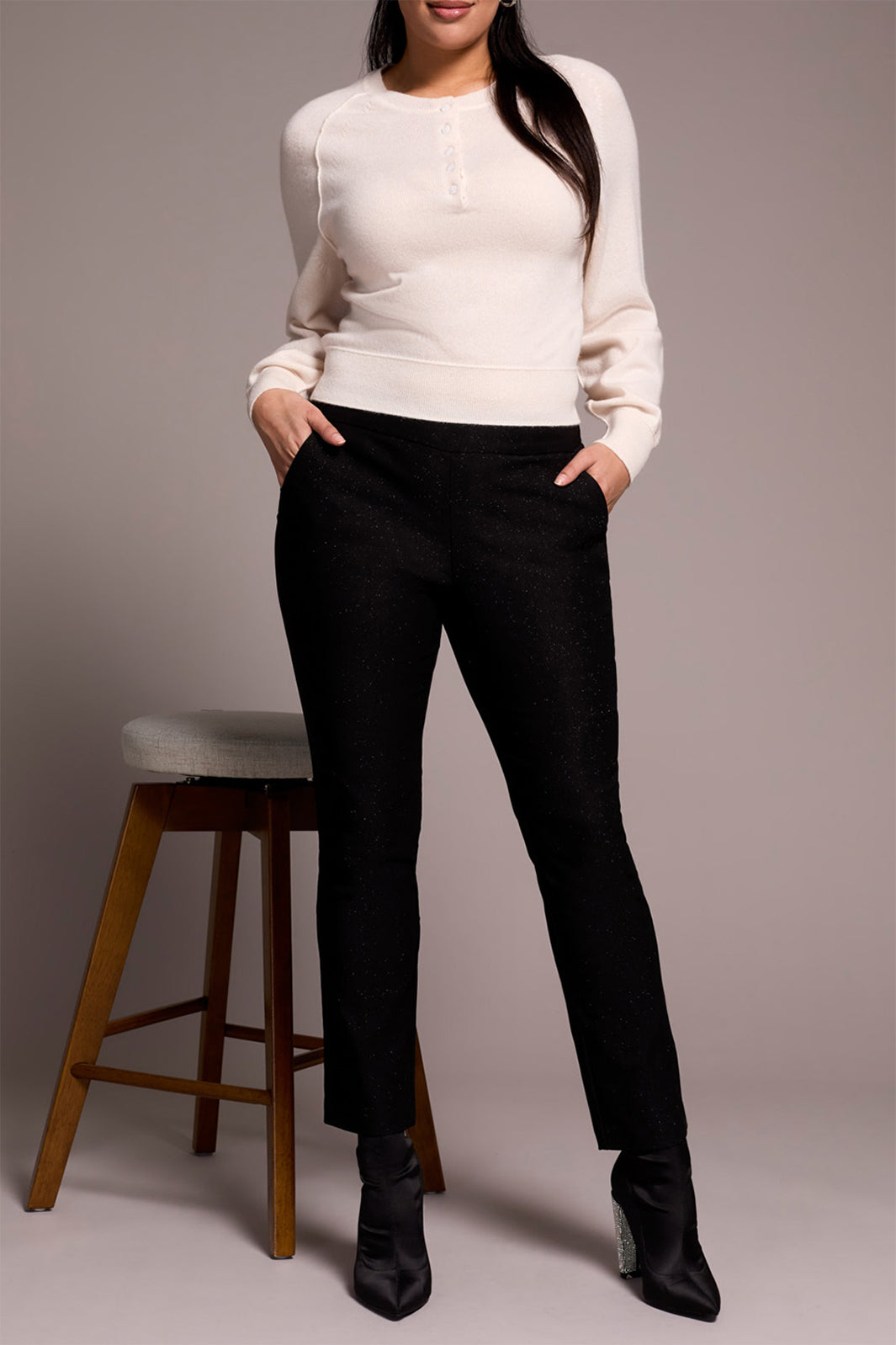 Person wearing a white sweater and black pants standing against a plain background