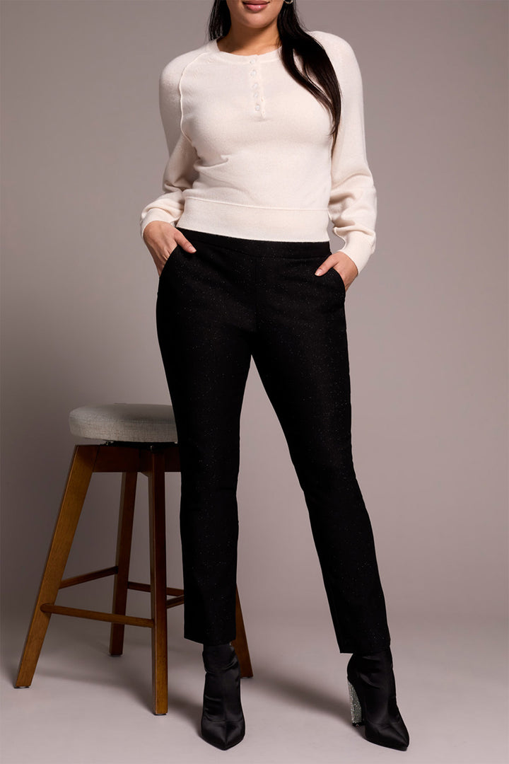 Person wearing a white sweater and black pants standing against a plain background