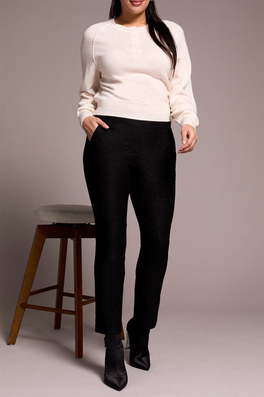 Person wearing a white sweater and black pants standing against a plain background