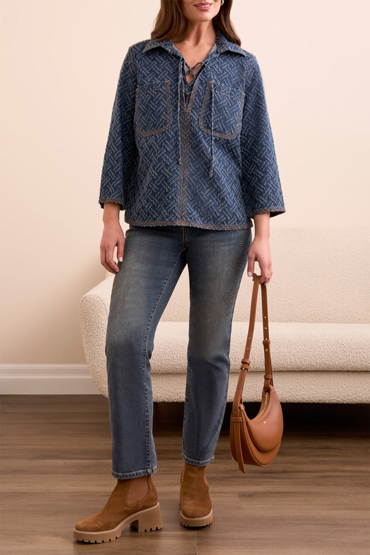 Woman wearing a blue denim shirt, jeans, and brown boots, holding a brown handbag indoors.