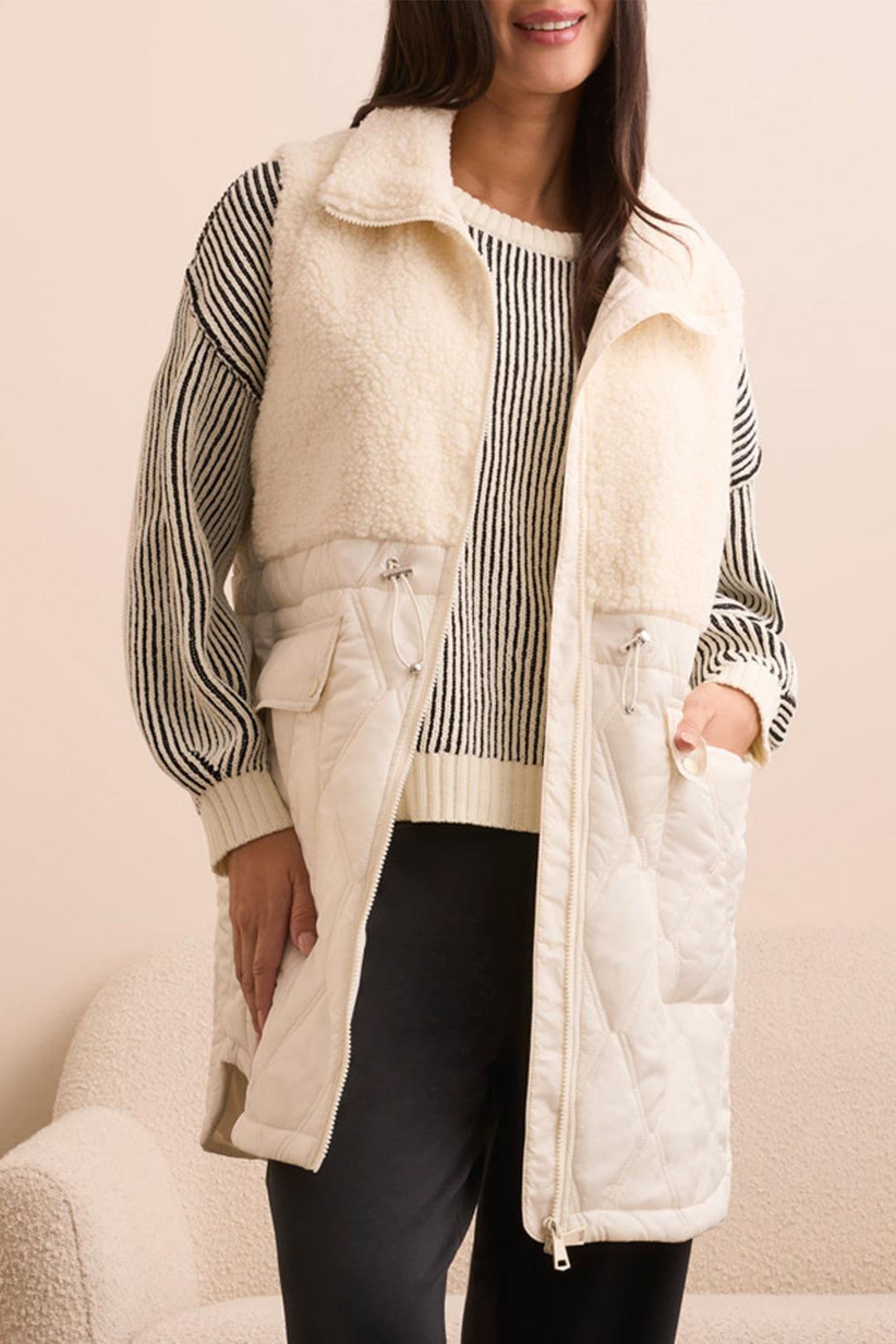 Person wearing a cream-colored puffer vest over a striped shirt with a neutral background