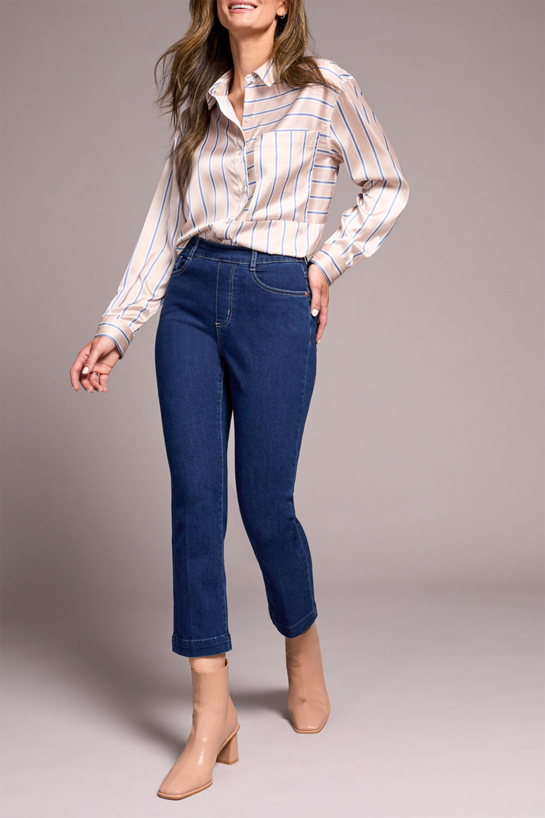 Woman wearing a striped shirt and blue jeans against a plain background