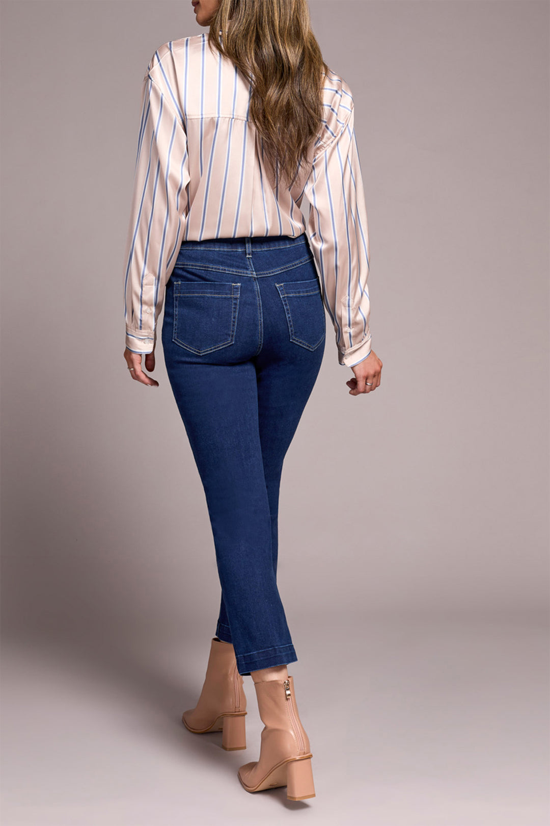 Woman wearing a striped shirt and blue jeans against a plain background